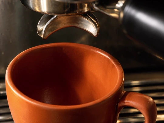 Espresso pouring into an orange ceramic cup